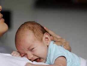 Madre recostada con su hijo llorando en sus brazos