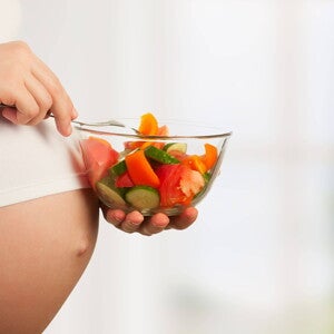 Mujer embarazada con un plato de verduras para hacer ensaladas.
