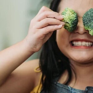 Niña jugando con dos brocolis